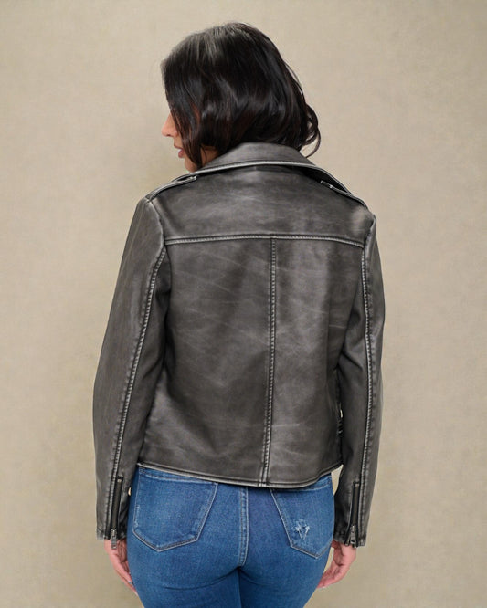 Person wearing a black leather jacket and blue jeans against a beige background