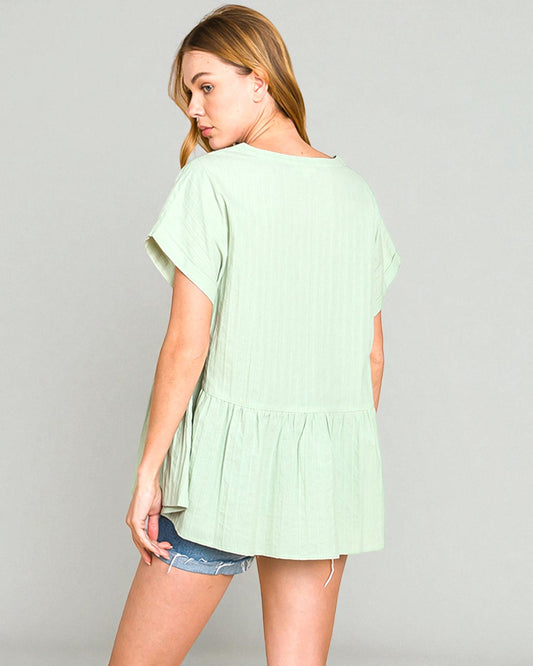 Woman wearing a light green blouse with ruffled sleeves on a gray background