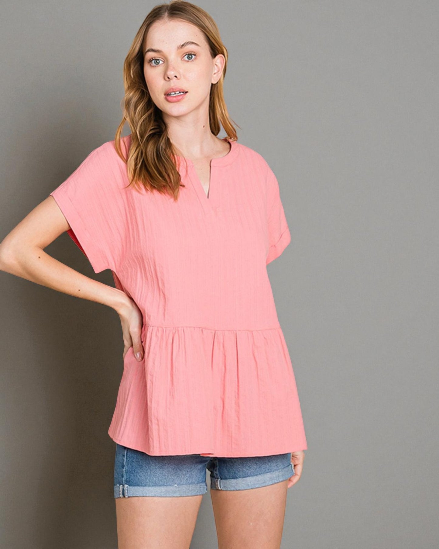 Woman wearing a pink blouse and denim shorts against a gray background