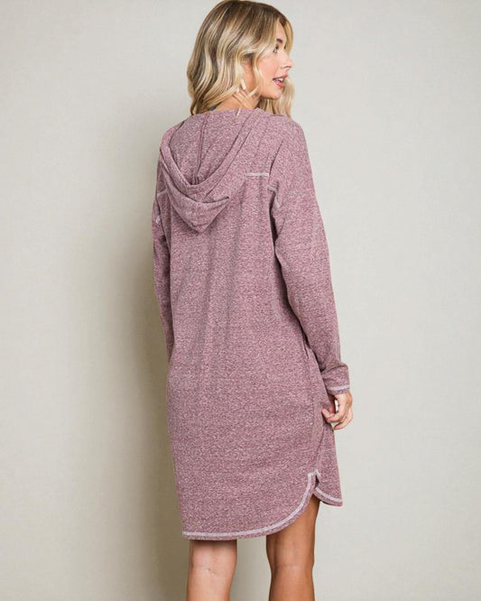 Woman wearing a mauve hooded dress against a plain background