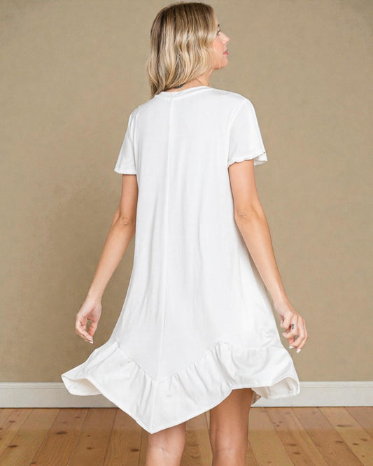 Woman wearing a white dress with ruffled hem against a beige wall.