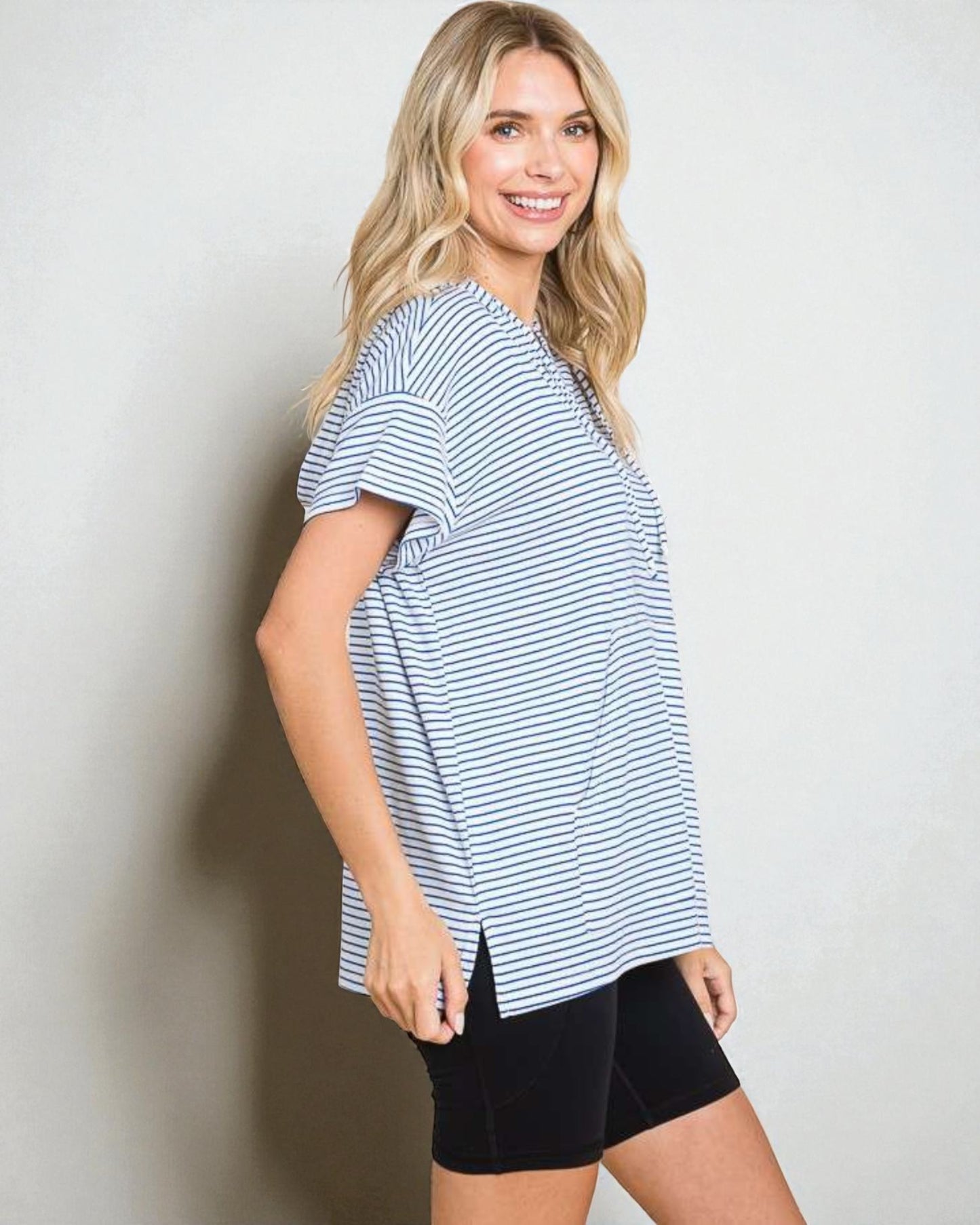 Woman wearing a blue and white striped shirt and black shorts against a plain background