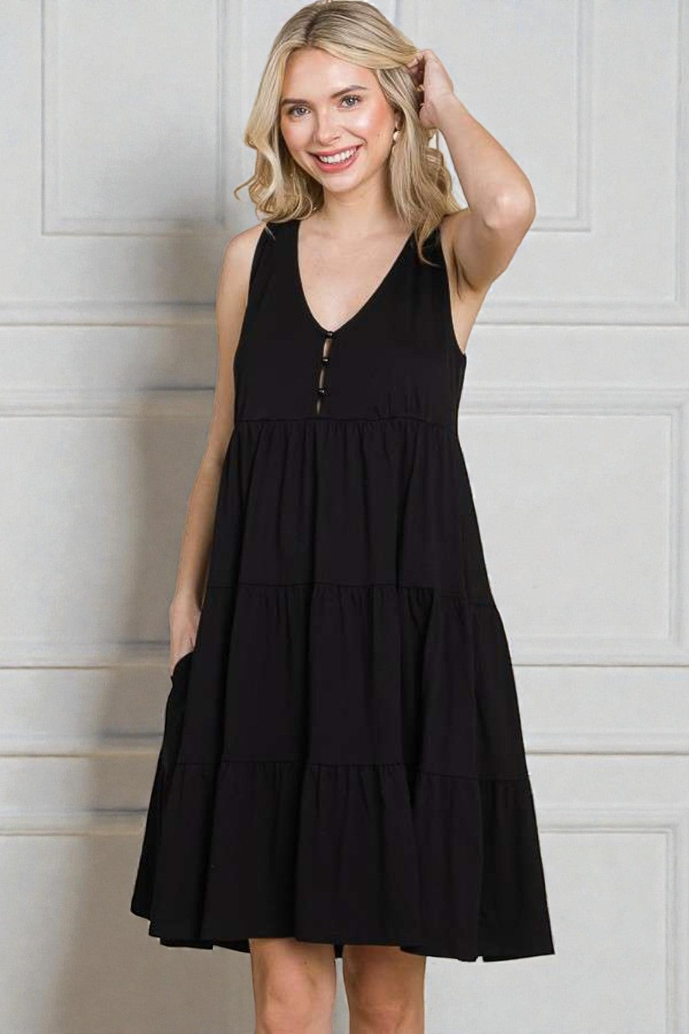 Woman wearing a black sleeveless dress against a white wall