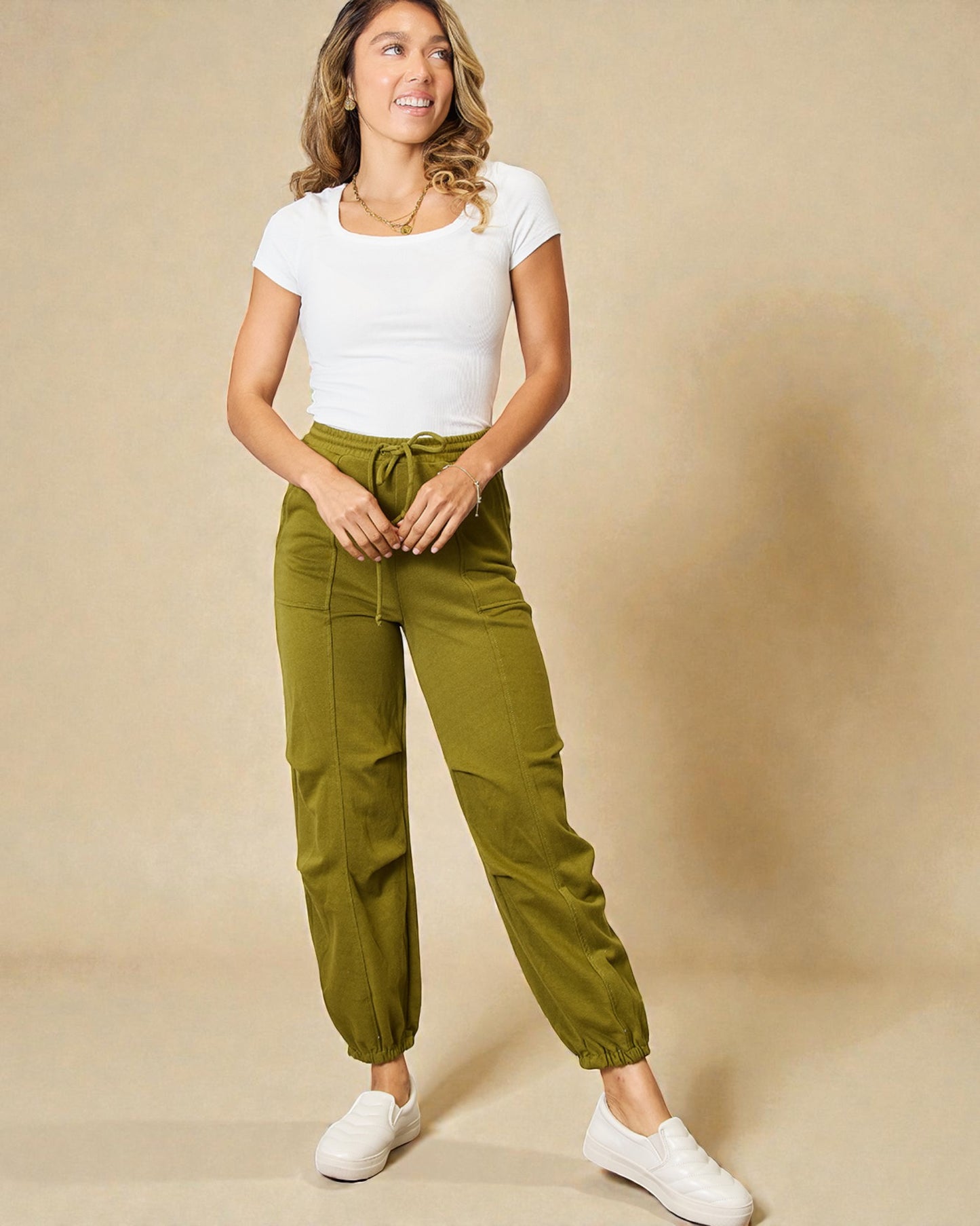 Woman wearing a white top and green pants against a beige background