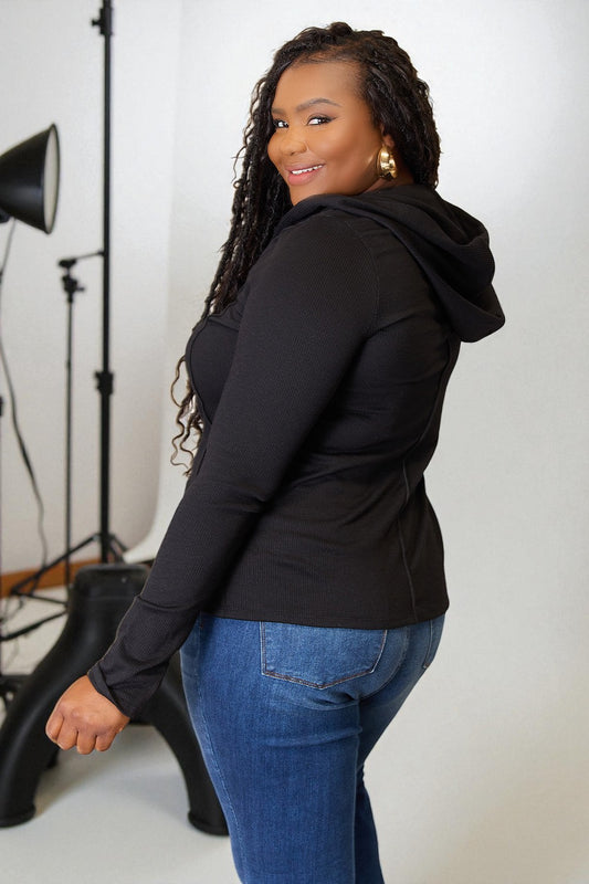 Woman wearing a black hoodie and blue jeans standing in a studio setting.