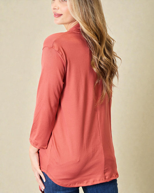 Woman wearing a rust-colored long-sleeve top against a beige background