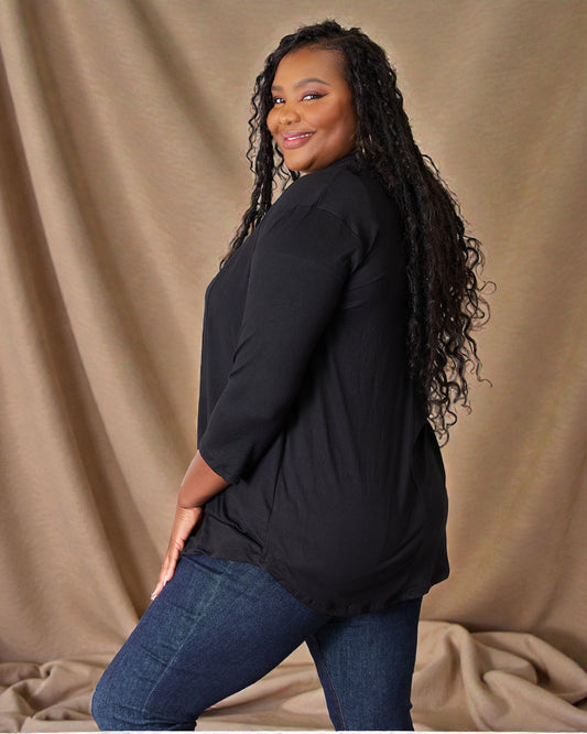 Woman wearing a black top and blue jeans against a beige background