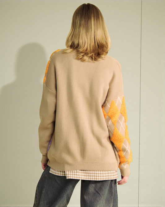 Person wearing a beige sweater with orange sleeves against a plain background