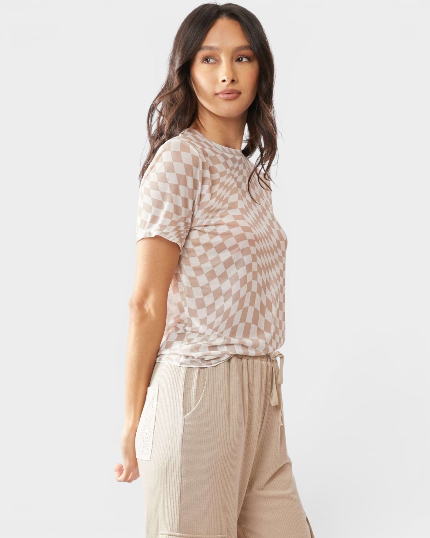 Woman wearing a checkered top and beige pants on a white background