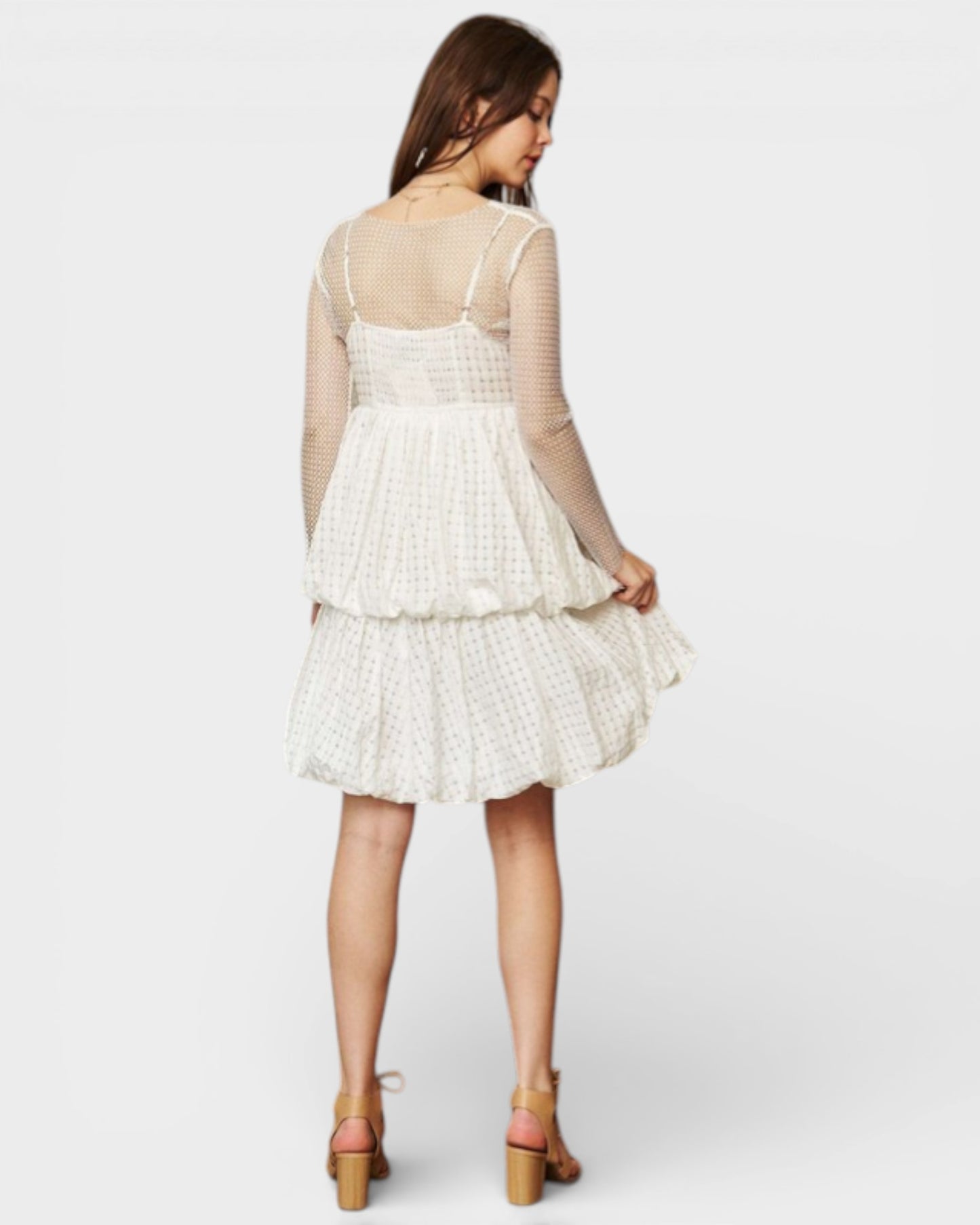 Woman wearing a white dress with sheer sleeves on a plain background