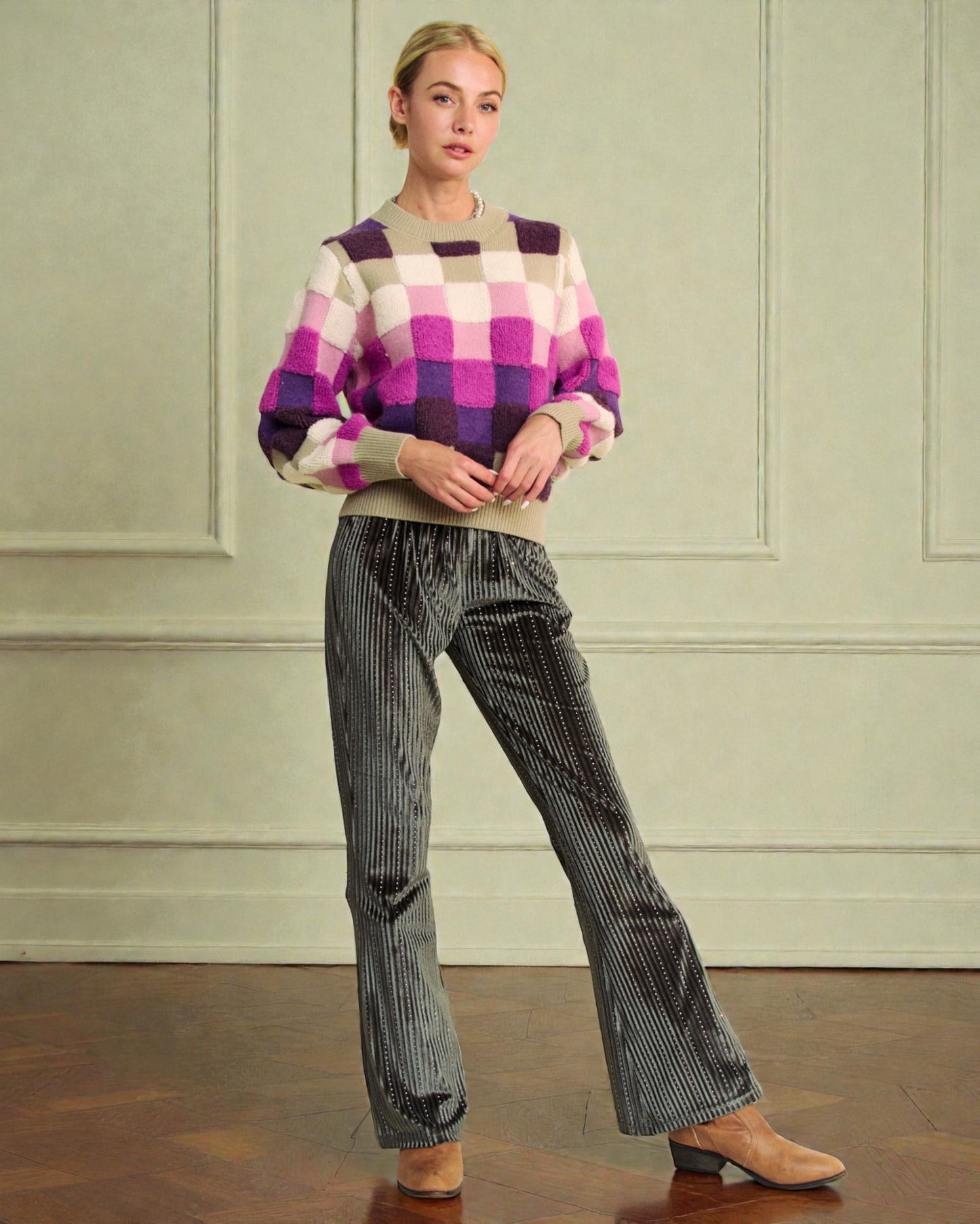 Woman wearing a checkered sweater and striped pants against a light green wall.