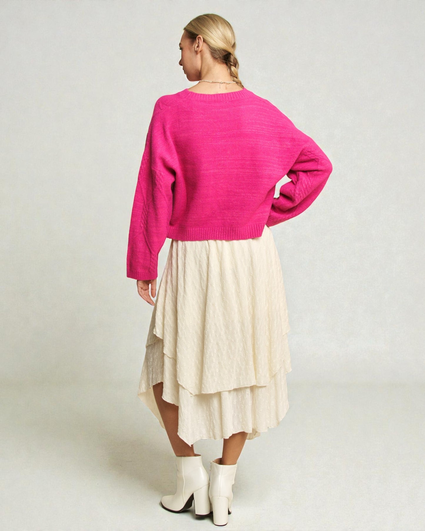 Person wearing a bright pink sweater and cream skirt on a plain background