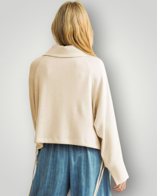 Person wearing a beige sweater and blue pants on a plain background