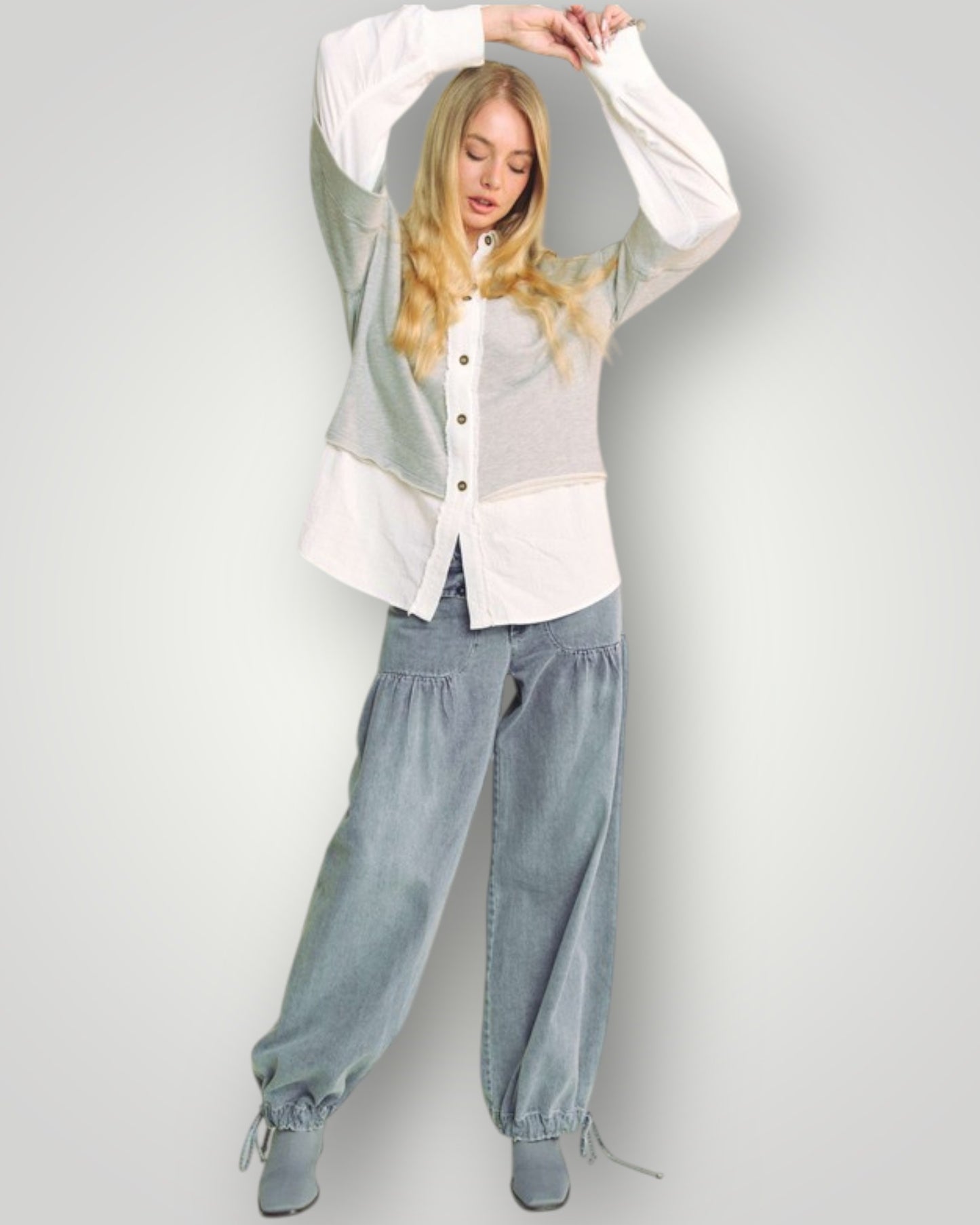 Woman wearing a layered outfit with a white shirt, green cardigan, and blue jeans on a plain background