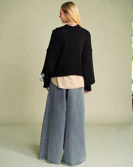 Person wearing a black sweater and gray wide-leg pants against a neutral background