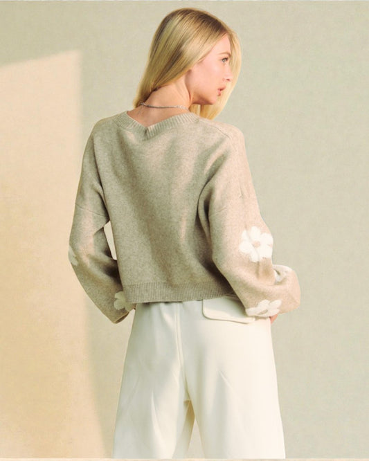 Person wearing a light green sweater and white pants holding a white bag against a beige background