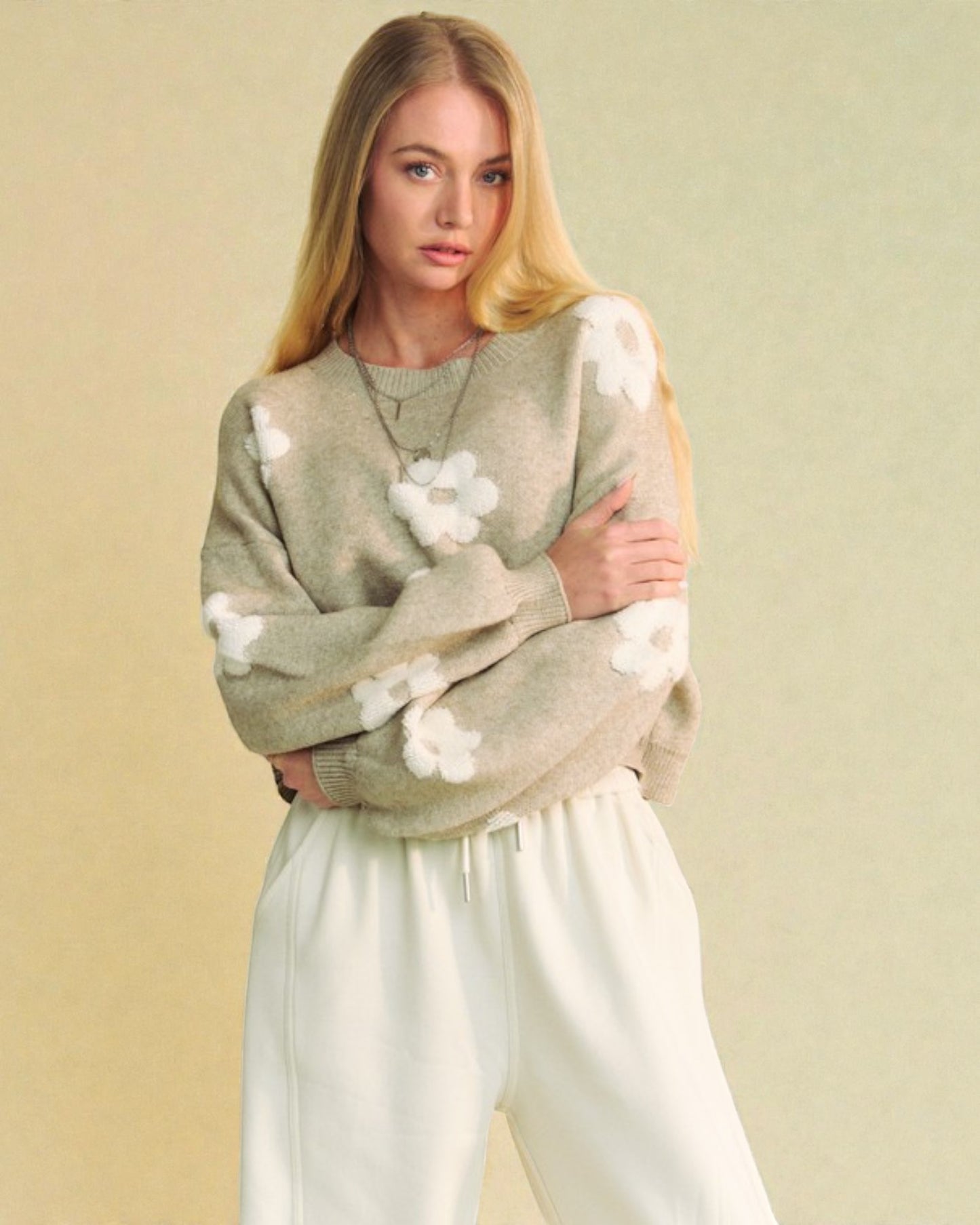 Woman wearing a green sweater with white floral patterns against a beige background