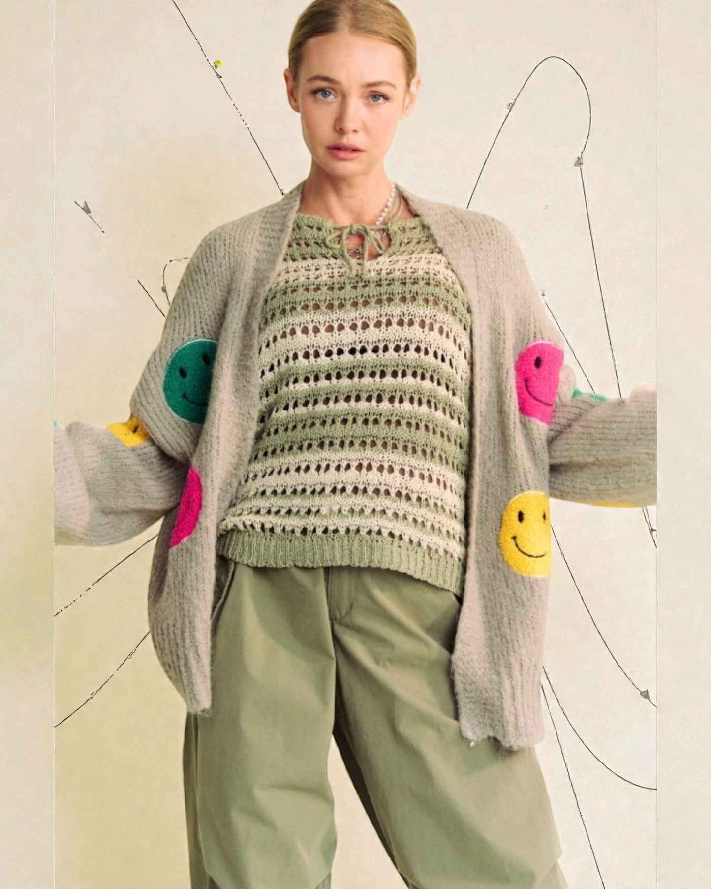 Woman wearing a green sweater with colorful smiley face buttons and a gray cardigan.