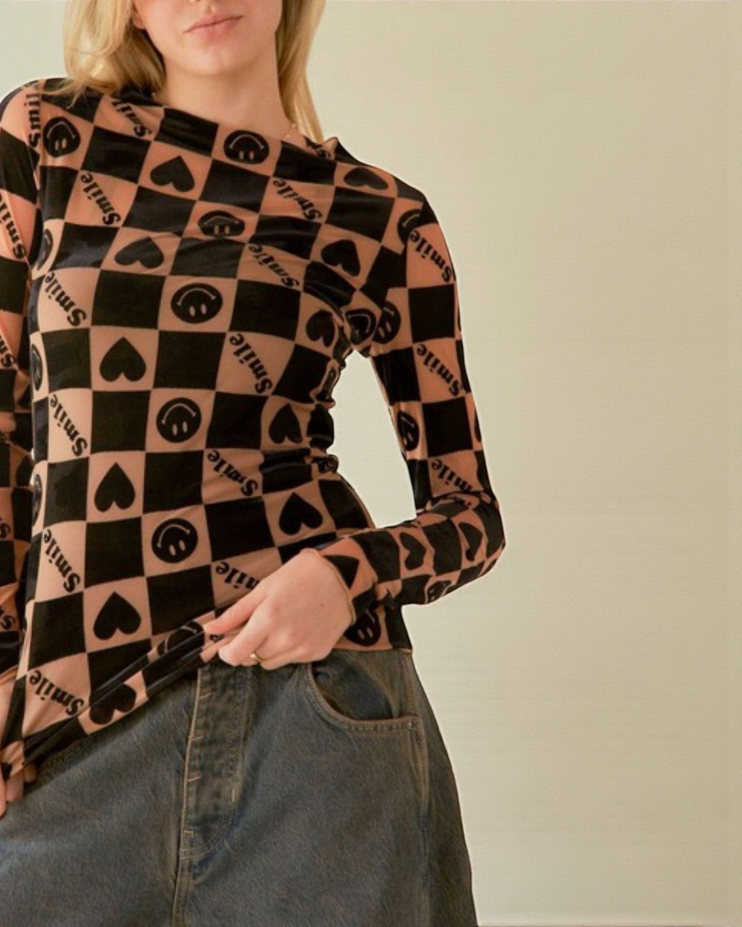 Person wearing a long-sleeve shirt with a pattern of hearts, squares, and text on a plain background