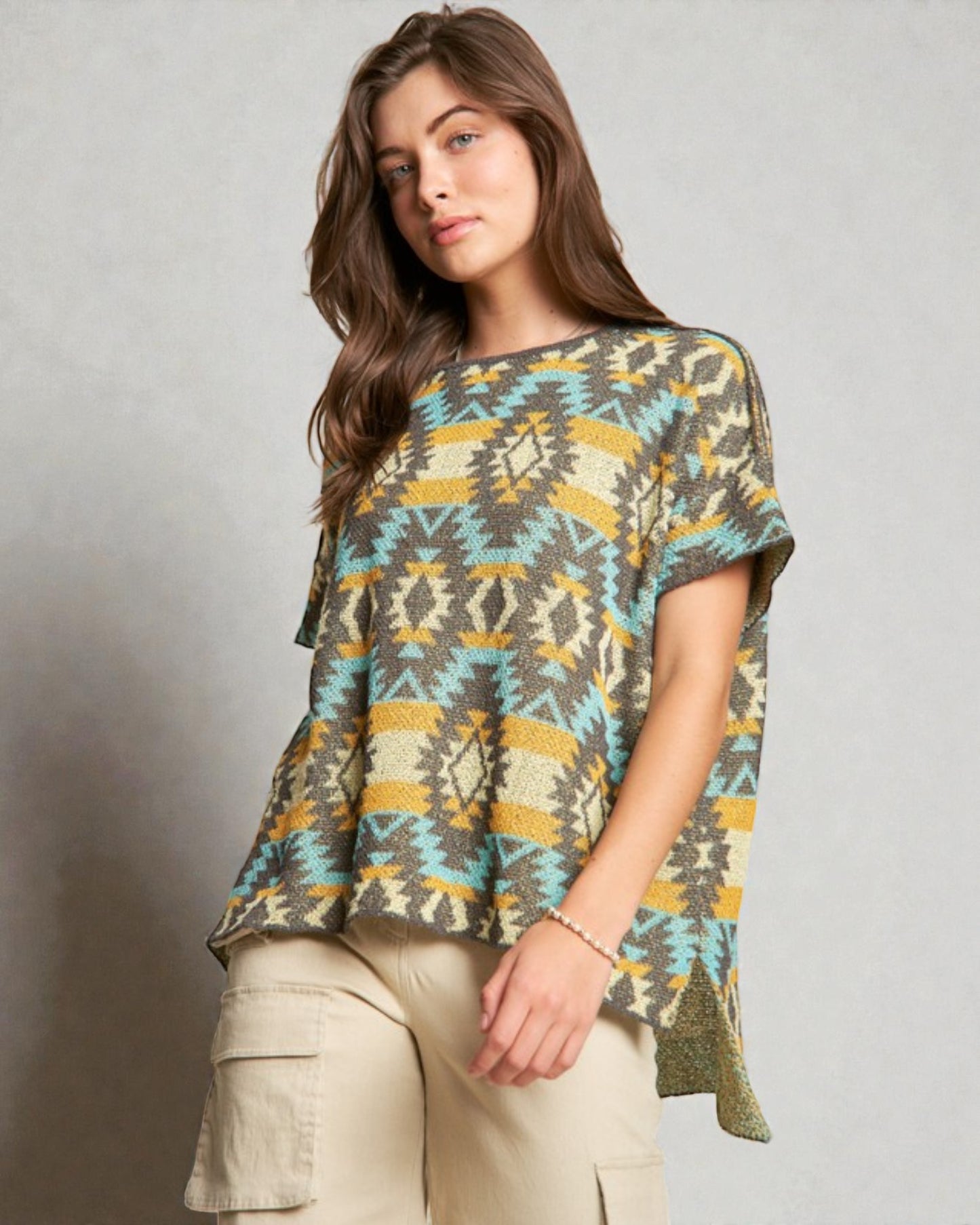 Woman wearing a patterned top and beige pants against a plain background