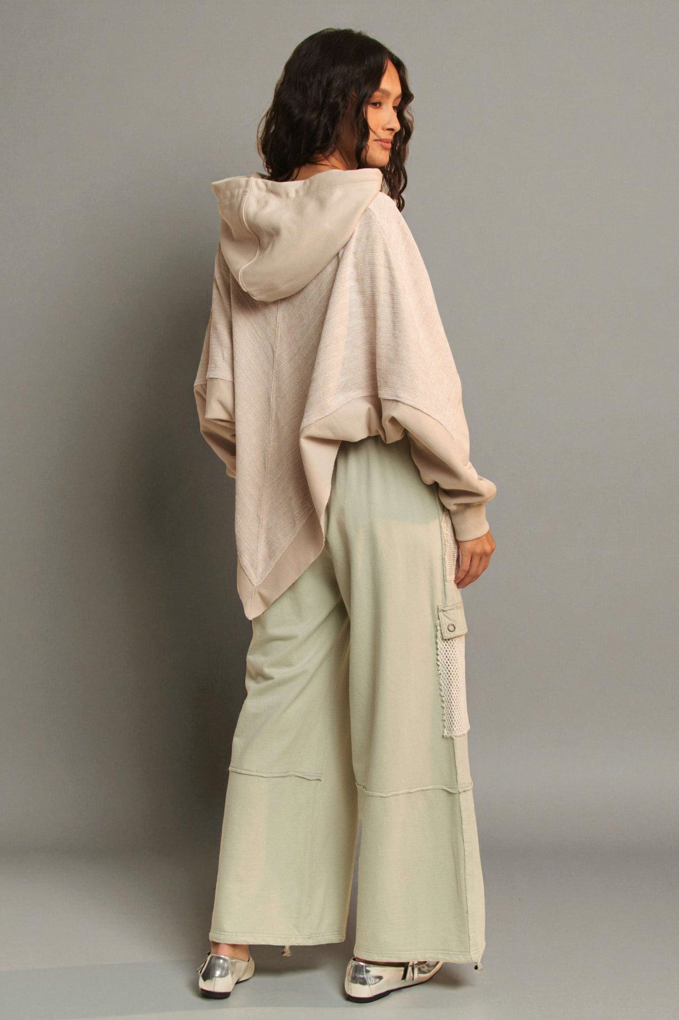 Woman wearing a beige hoodie and light green pants against a gray background