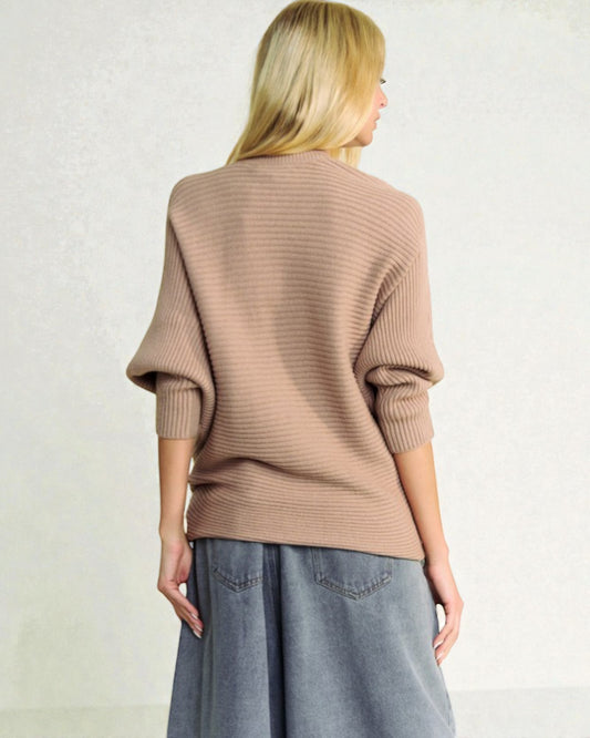 Person wearing a beige sweater and gray pants against a plain background