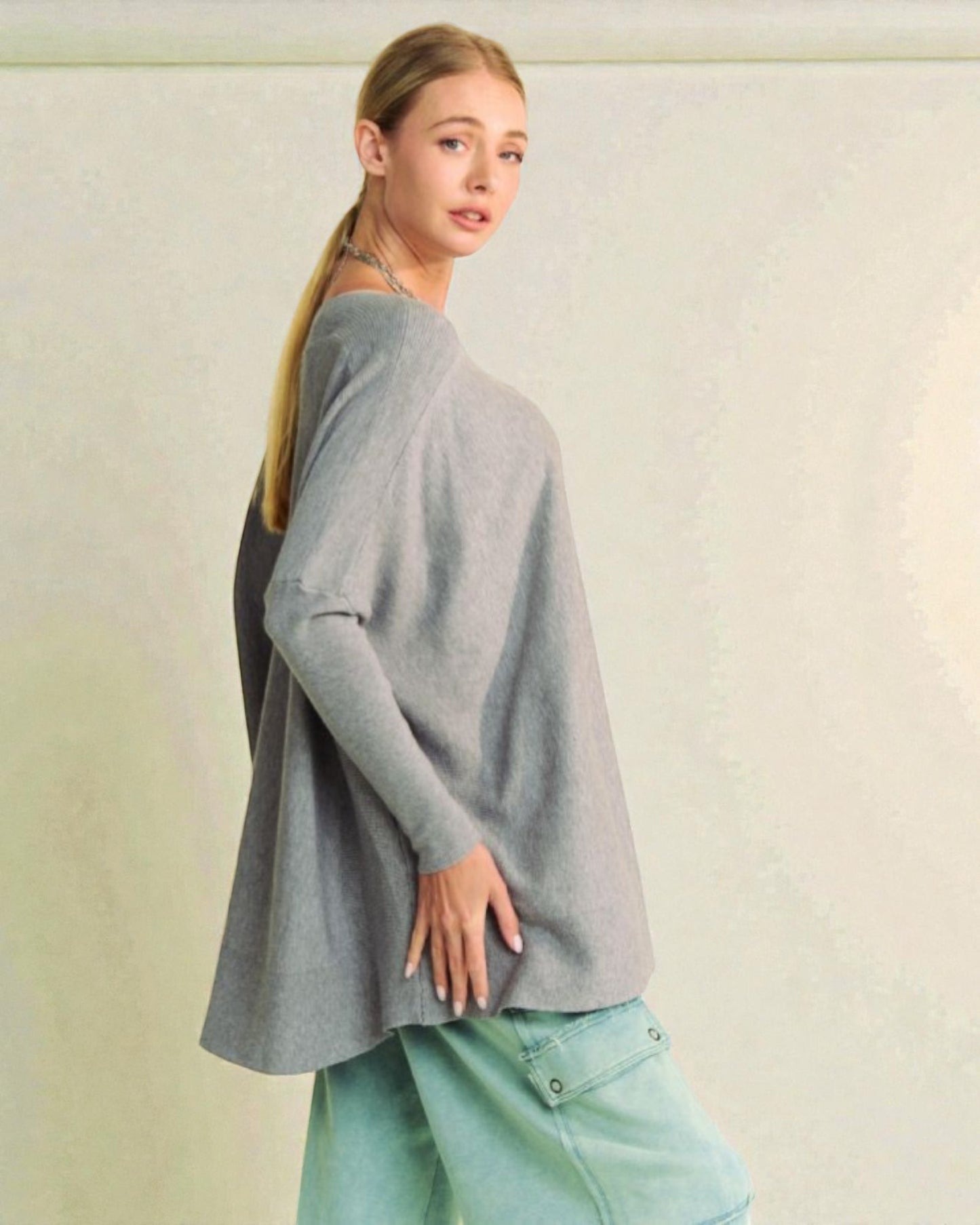 Woman wearing a gray sweater and light blue jeans against a plain background