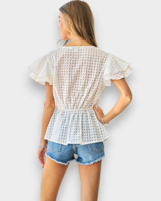 Woman wearing a white lace top and denim shorts against a white background