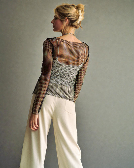 Woman wearing a mesh top and white pants against a plain background