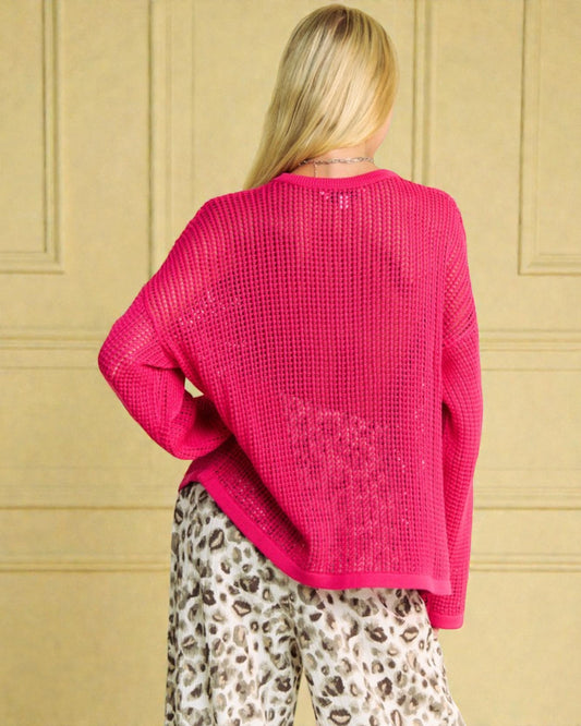 Person wearing a bright pink sweater and leopard print pants against a beige wall.