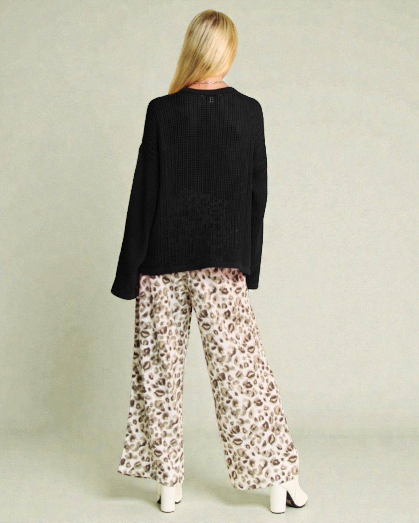 Person wearing a black sweater and leopard print pants on a plain background