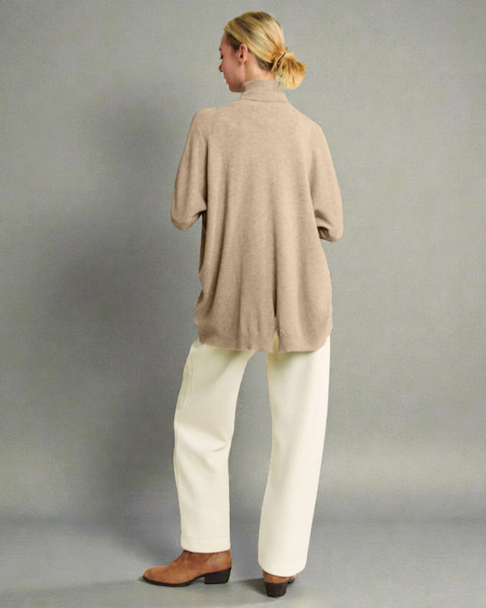 Person wearing a beige sweater and white pants against a gray background
