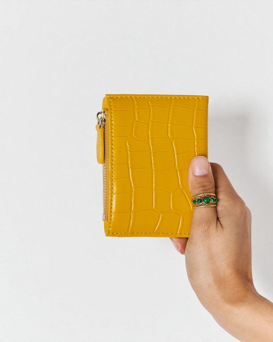 Hand holding a mustard yellow crocodile texture wallet against a light gray background