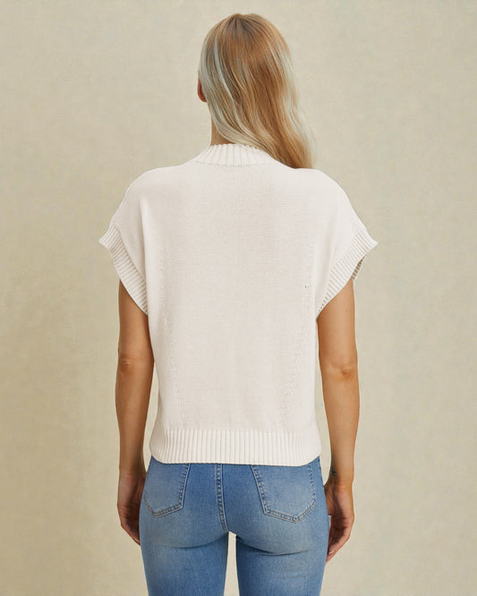 Person wearing a white sleeveless sweater and blue jeans on a beige background