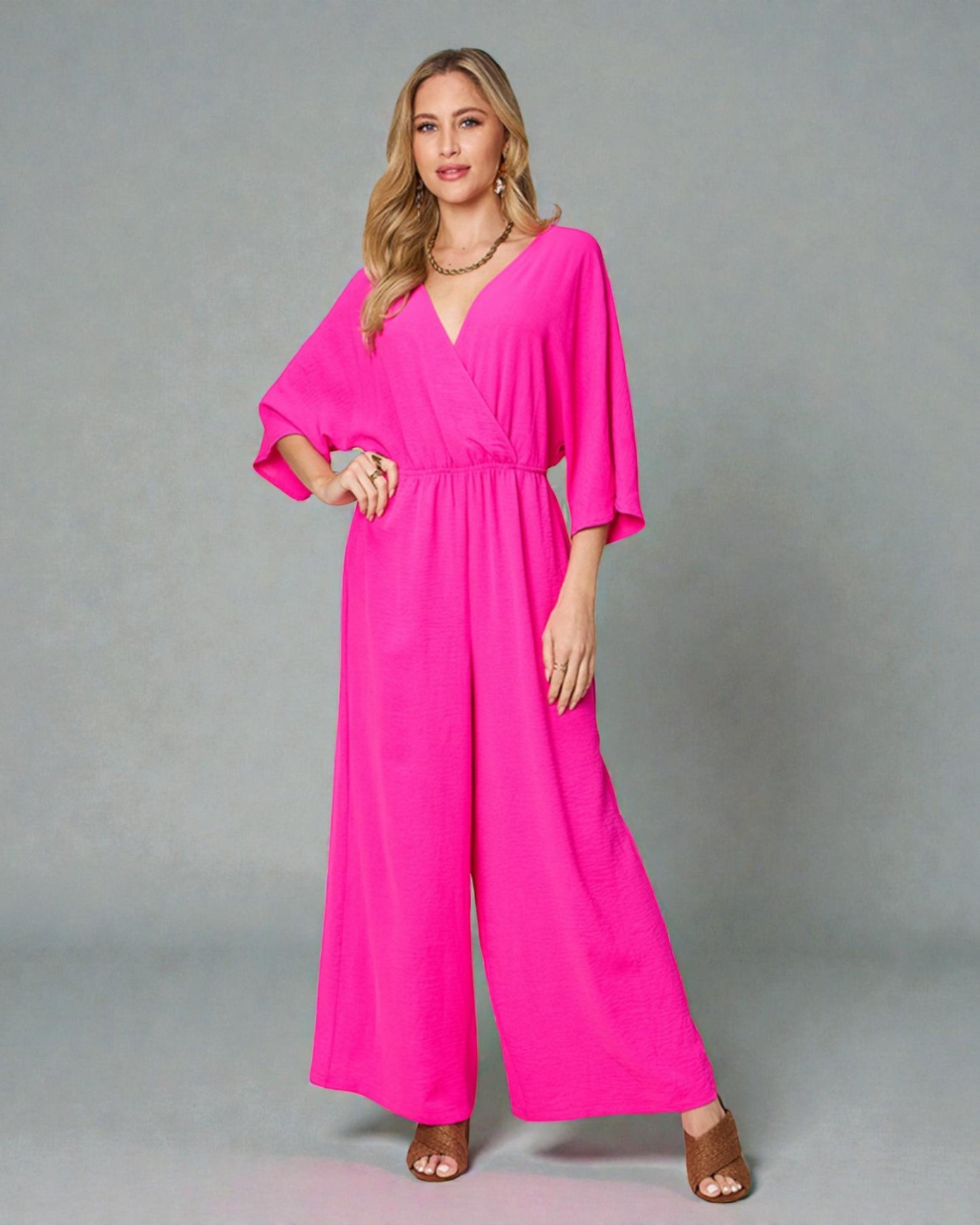 Woman wearing a bright pink jumpsuit on a gray background
