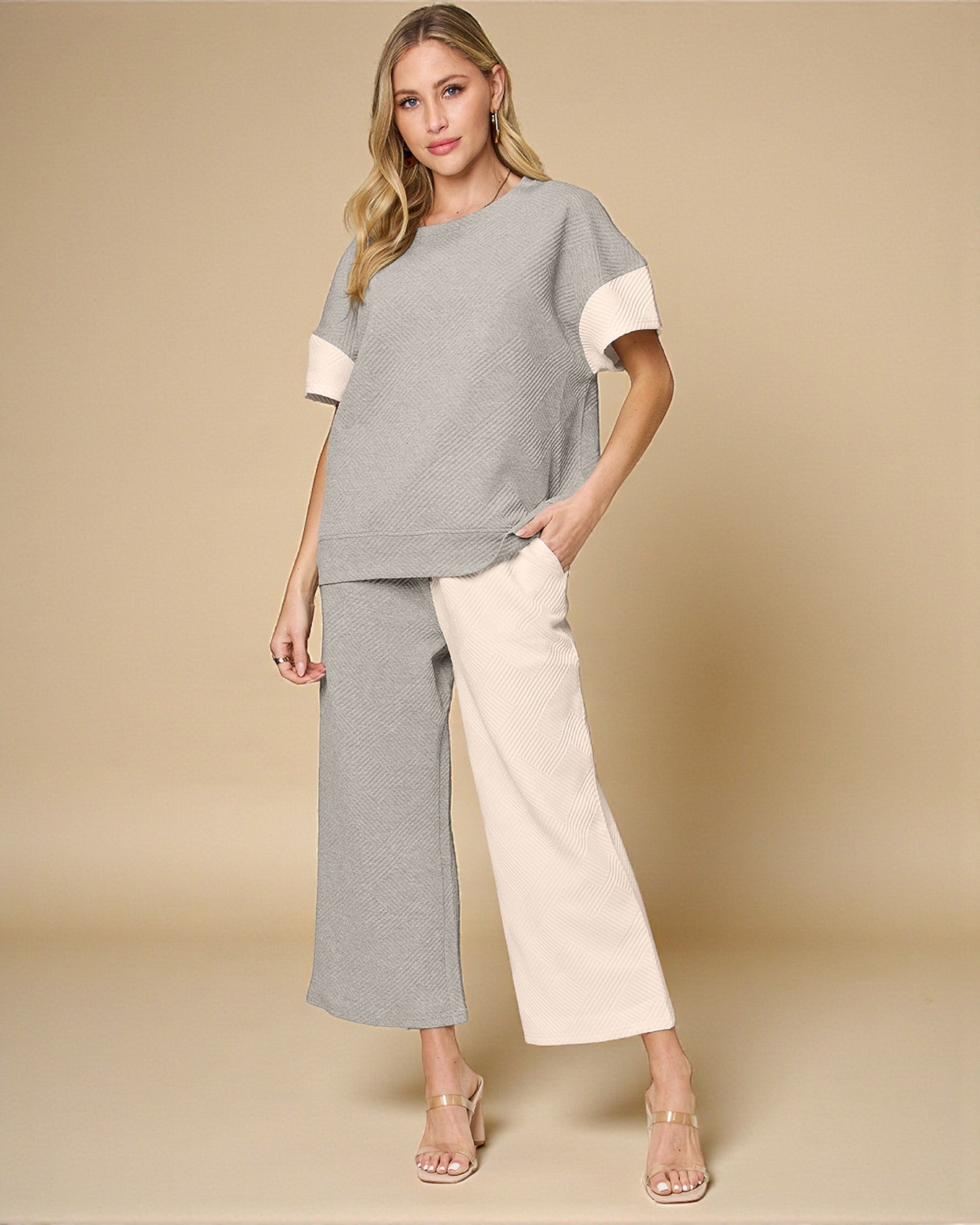 Woman wearing a gray and white outfit with beige pants on a beige background