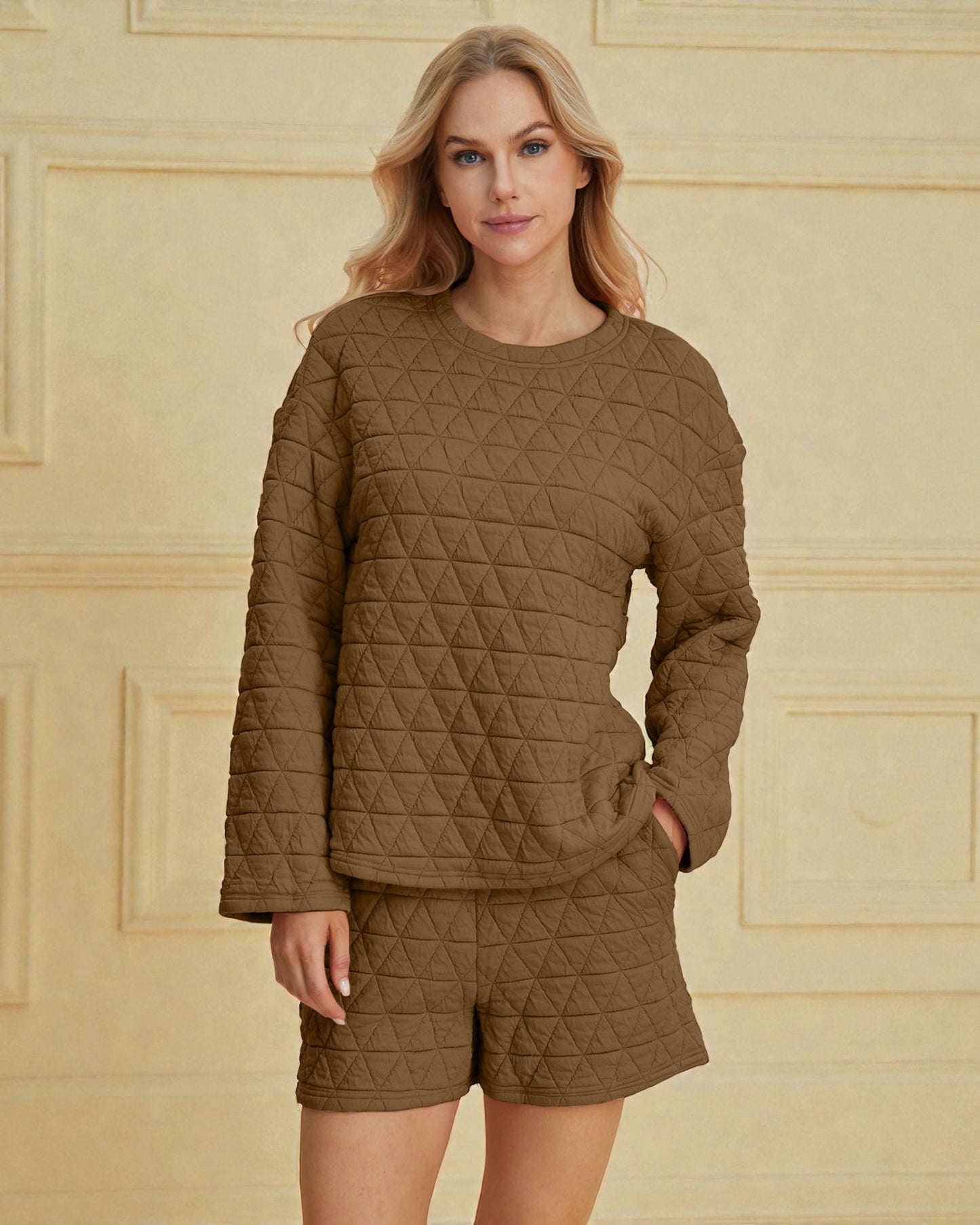 Woman wearing a brown quilted outfit against a beige wall.