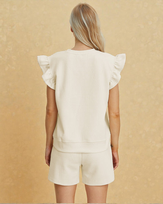 Person wearing a cream-colored outfit with ruffled sleeves on a beige background