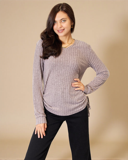 Woman wearing a gray ribbed sweater and black pants against a beige background