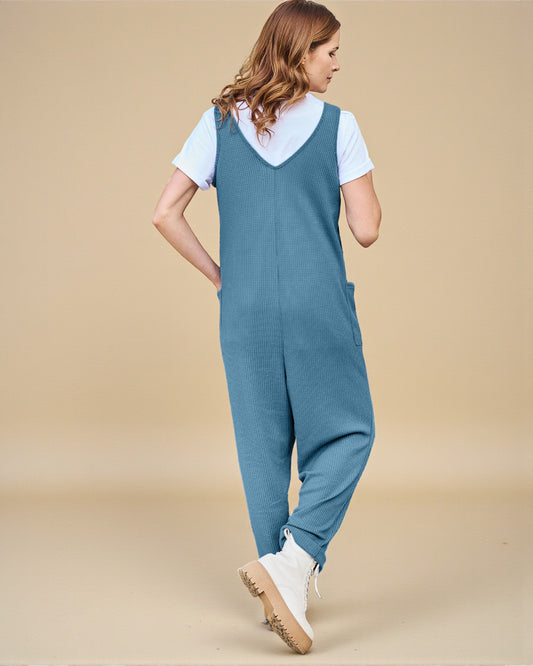 Woman wearing a blue denim overalls with a white shirt underneath on a beige background