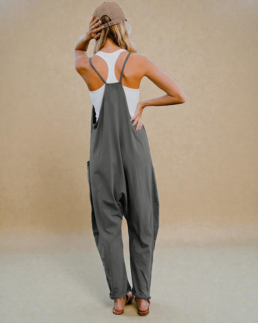 Woman wearing a gray jumpsuit and white tank top against a beige background