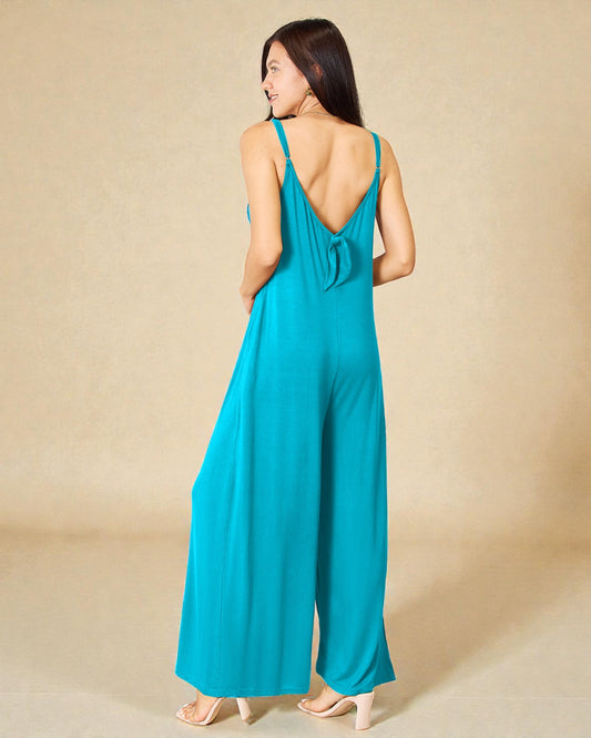 Woman wearing a turquoise jumpsuit with an open back on a beige background