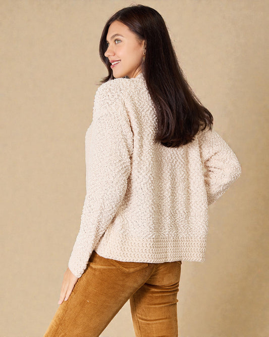 Woman wearing a beige textured sweater and brown pants against a beige background