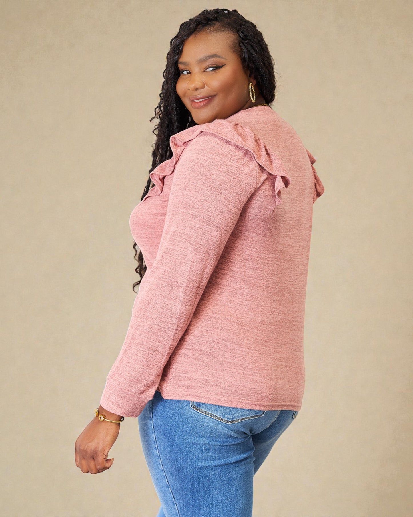 Woman wearing a pink sweater with ruffled shoulders against a beige background