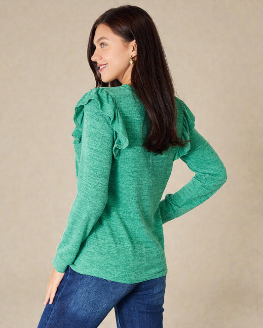 Woman wearing a green sweater with ruffled shoulders against a beige background