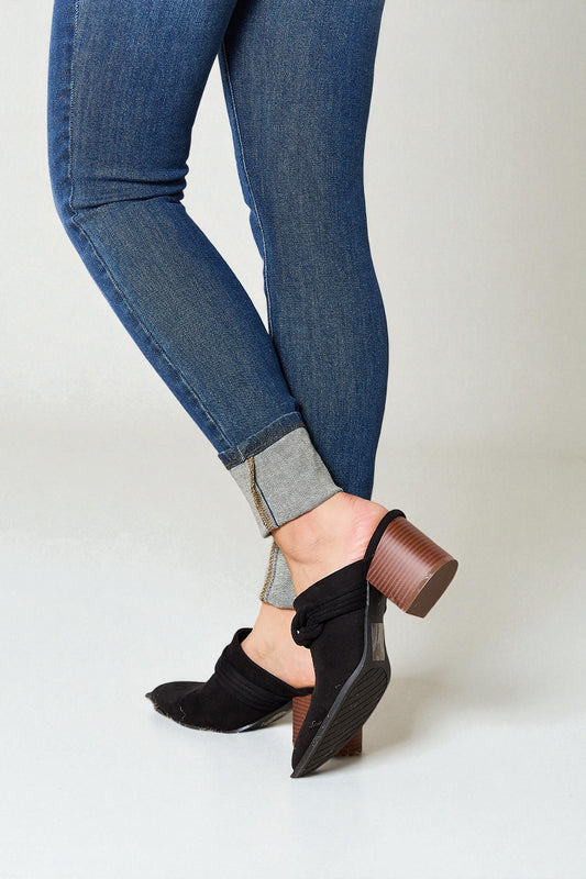 Person wearing blue jeans and black clogs on a white background