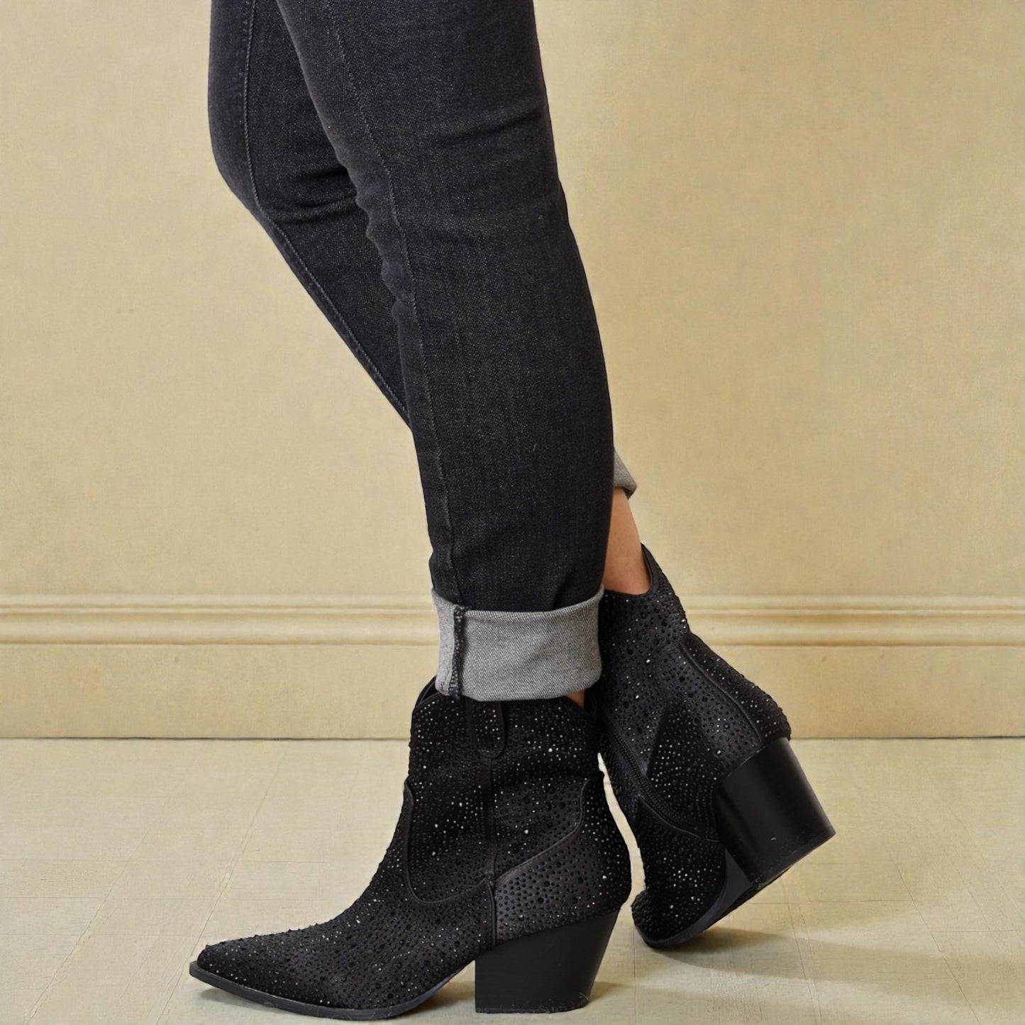 Black ankle boots worn with black jeans on a beige background