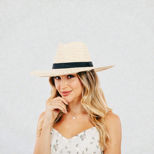Woman wearing a straw hat with a black band on a plain background