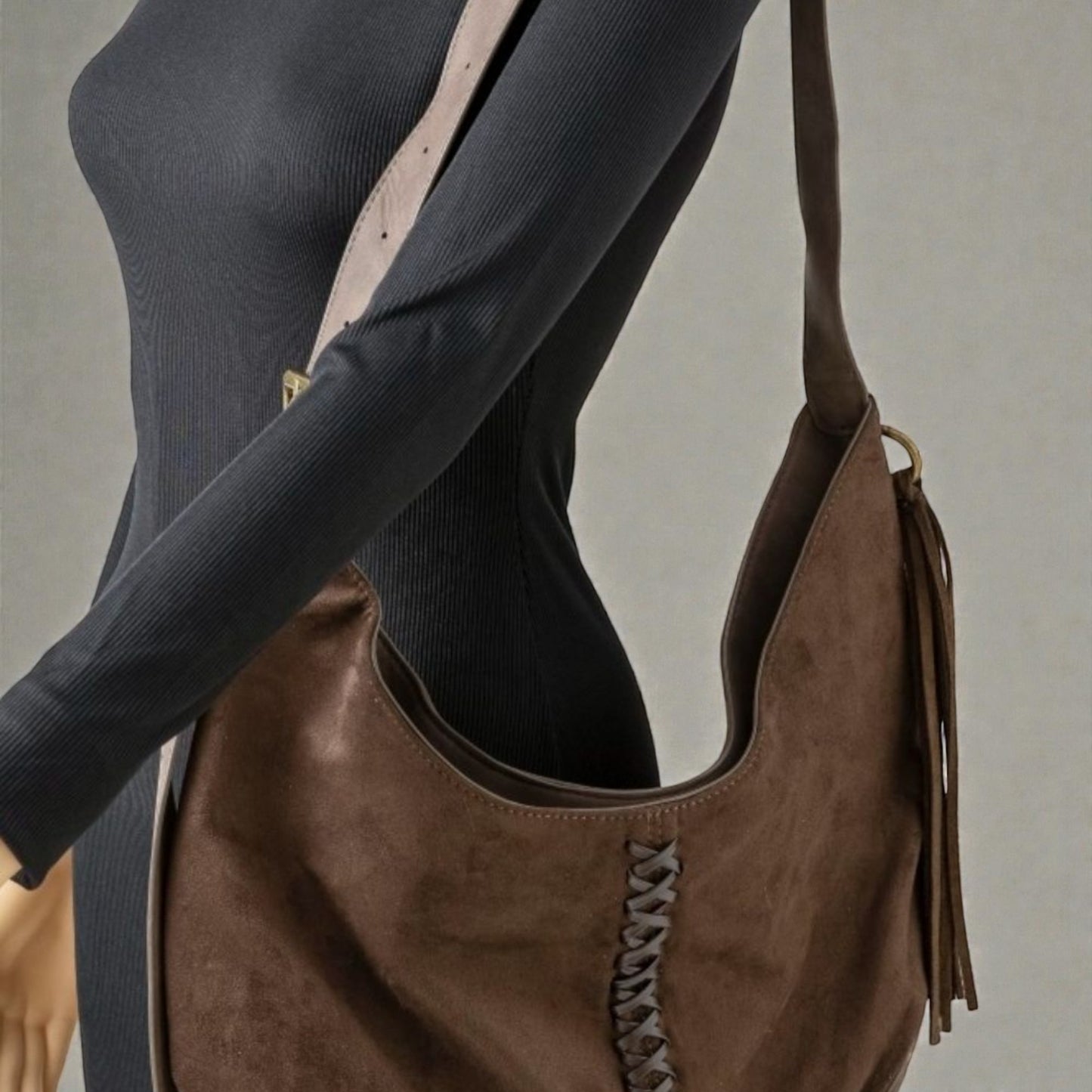 Brown leather handbag with tassels held by a person wearing a black outfit.