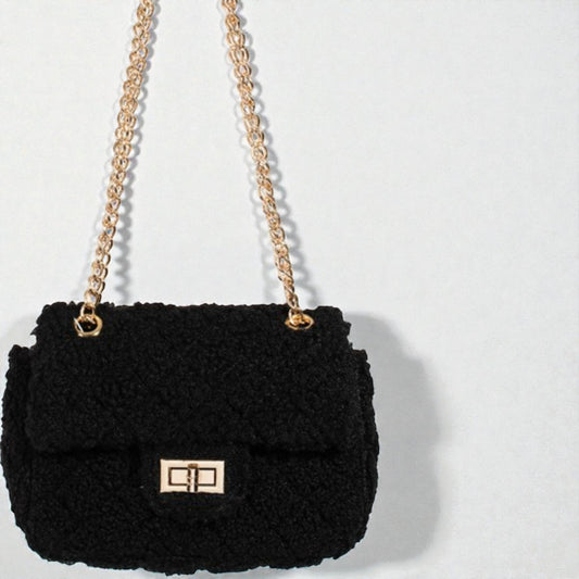 Black textured handbag with gold chain strap on a light gray background